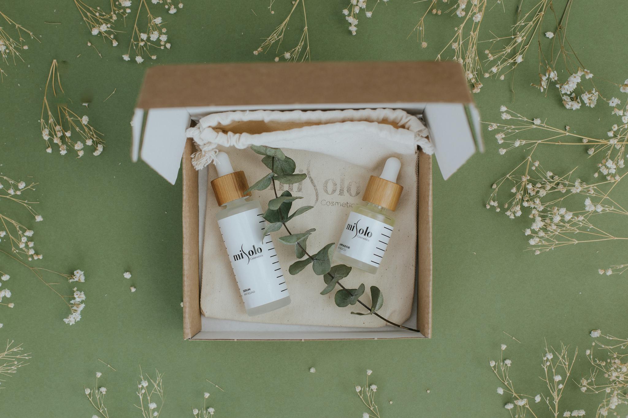 A beautifully arranged skincare set in eco-friendly packaging with dried flowers and eucalyptus on a green background.